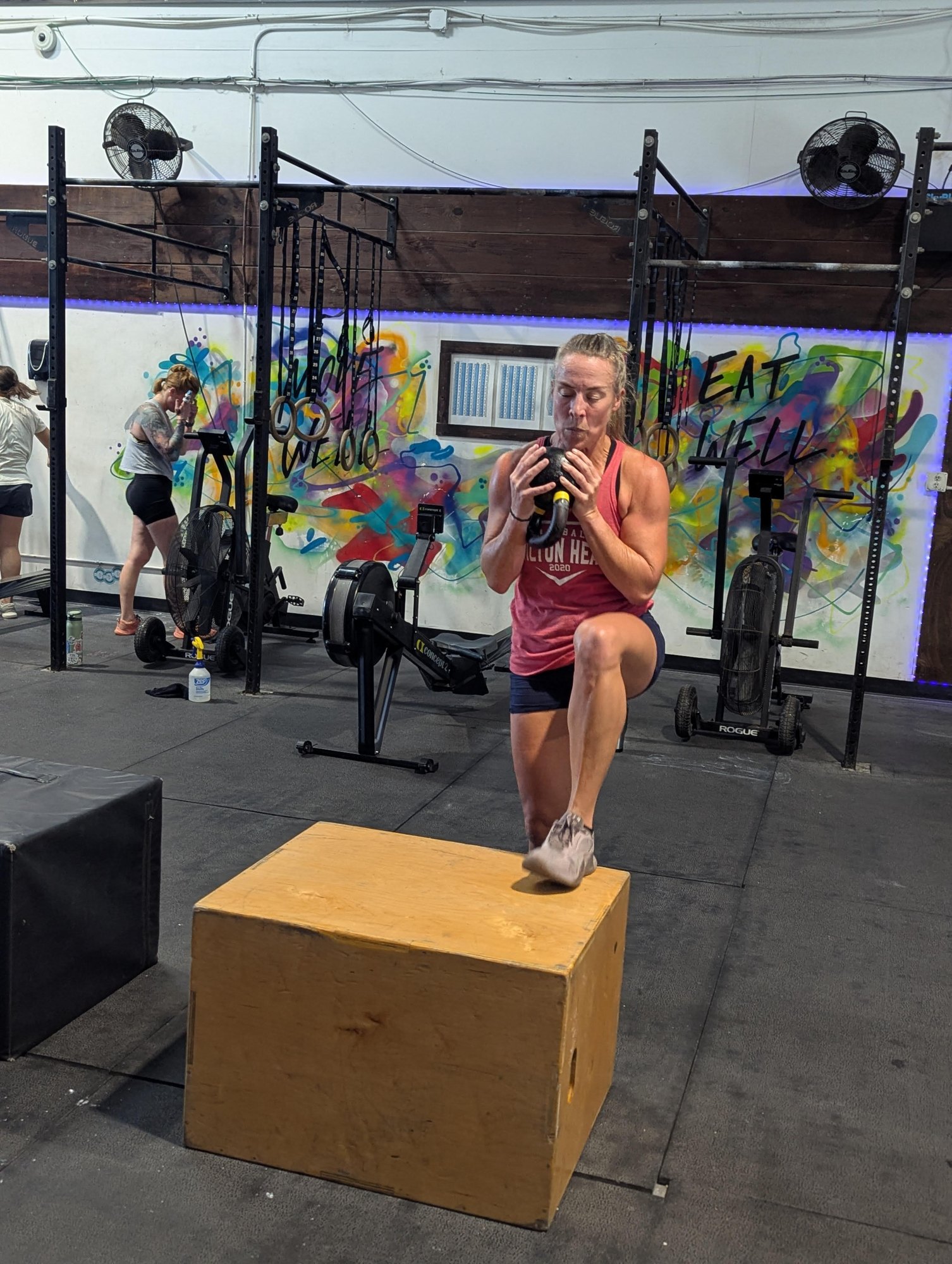 A Nomad Fitness member practicing a weighted step-up in front of the Move Well and Eat Well mural